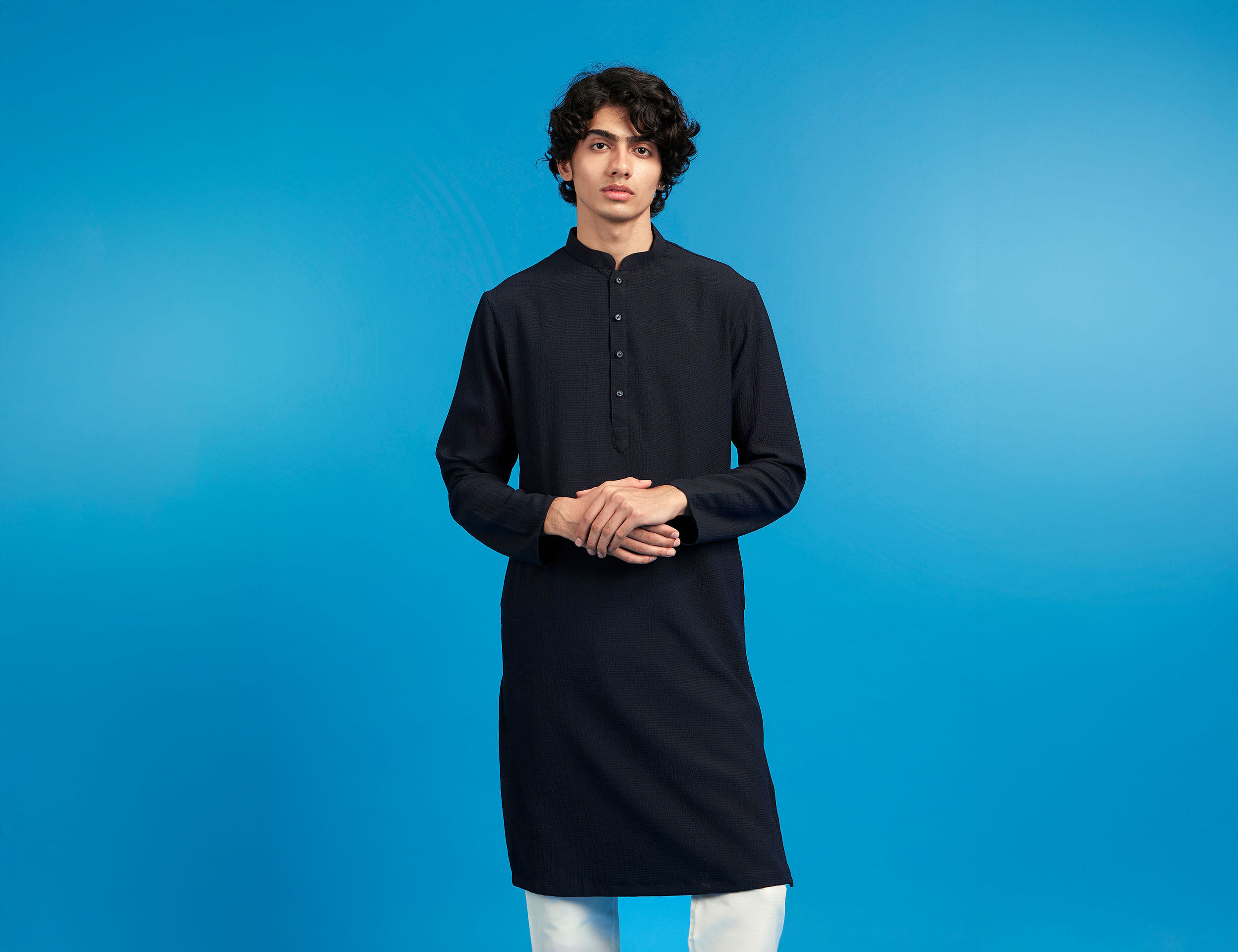 Young man in a classic black kurta and white churidar, posing confidently against a solid blue background.